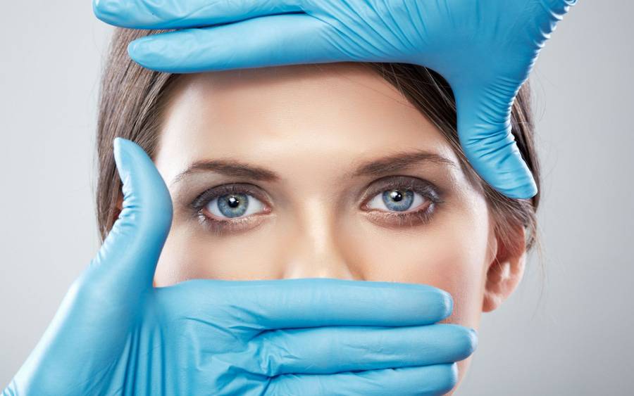 A woman's face is covered by gloved hands of plastic surgeon