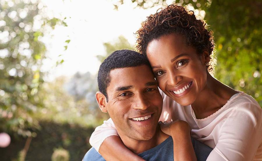 A smiling middle-aged woman and man cuddle close to each other, representing the enhanced appearance and confidence after facelift, rhinoplasty or otoplasty.