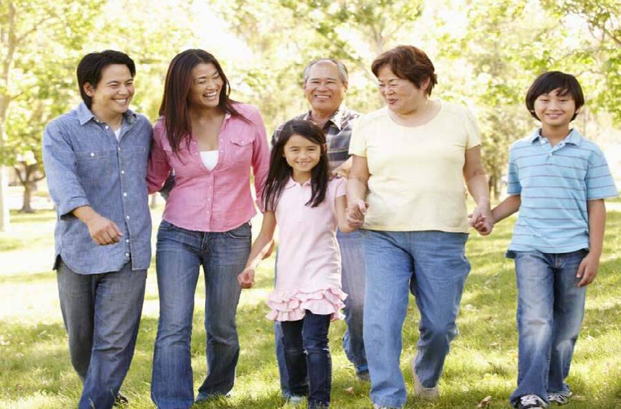 A multigenerational Asian family smiles as they take a walk together outdoors.