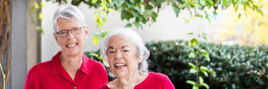 Two women stand and smile while wearing red in a bright, sunny area, representing how cardiac rehab at Scripps helped them get back to good health.