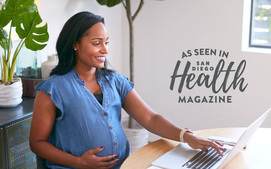 A young black woman smiles as she searches on the computer to look for a pediatrician before her baby is born - SD Health Magazine