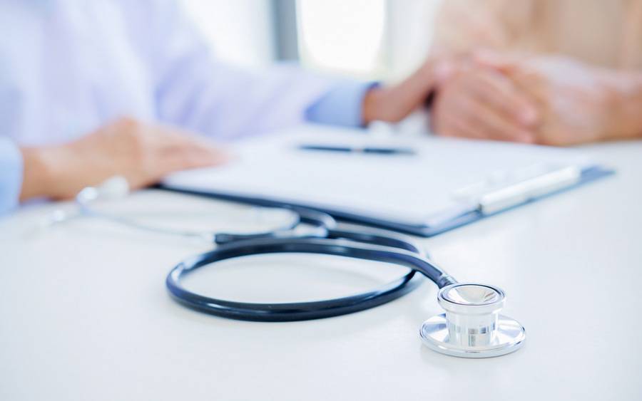 A close-up photo shows a stethoscope and clipboard on a desk, with a physician's hands and patient's hands in the background.