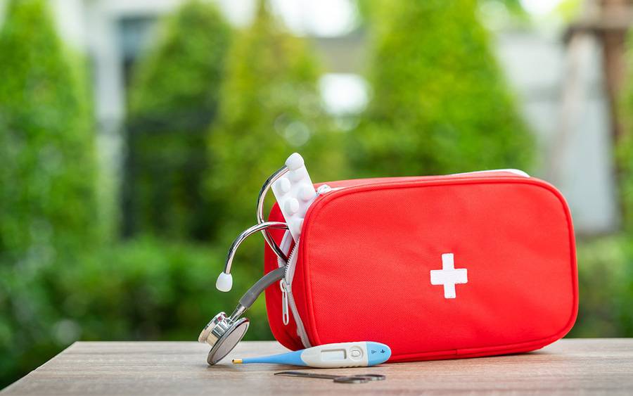 A red first aid kit with thermometer and other first aid supplies.