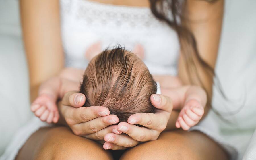 Mother holds baby's head checking for signs of flat head syndrome.