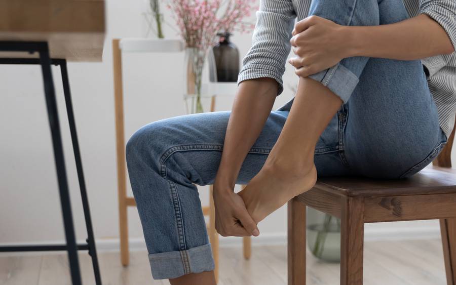 a woman grabs her bare foot in pain.