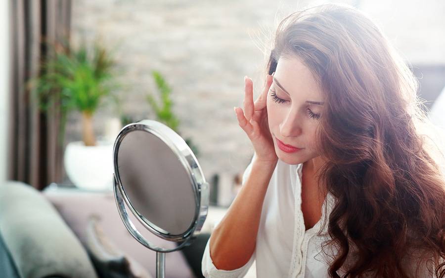 A woman looks at her face in the mirror after undergoing a cosmetic dermatology procedure.