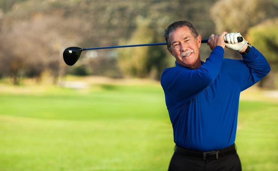 Scripps patient Garry Collins stands on a golf course swinging a golf club.