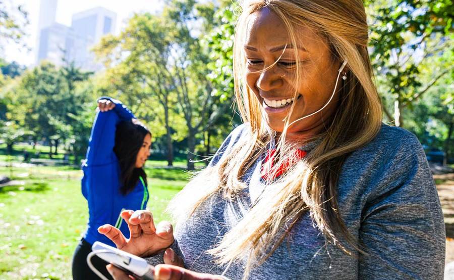 A woman with a mobile device wearing headphones preparing to exercise outdoors, representing the active lifestyle that people often enjoy after gastric sleeve surgery.