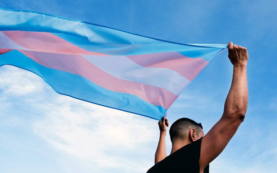 A transgender man holds up the transgender flag.