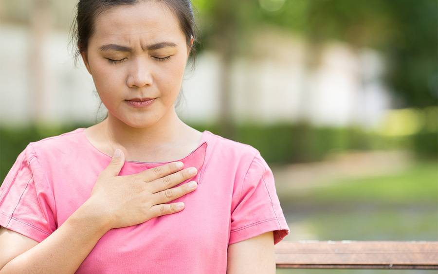 A young Asian-American woman grabs her chest wondering if she has heartburn or GERD or something else.
