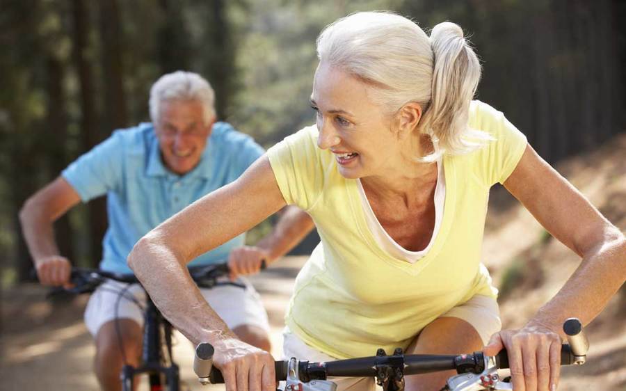 An older couple exercises on their mountain bikes outdoors to help prevent deep vein thrombosis.
