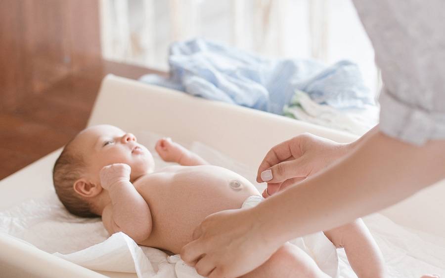 A mother changes the diaper of a newborn baby on a changing table, representing the essential parenting skills learned in this class.