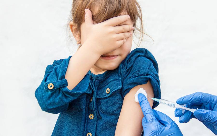 A little girl covers her eyes as she gets a vaccine injection.