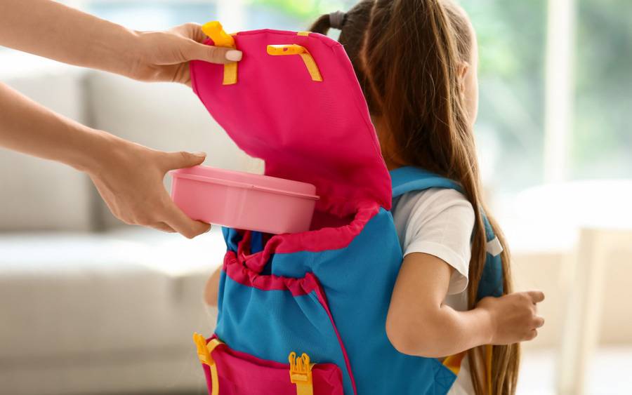 Mom packs a healthy lunch into her daughter's backpack. 