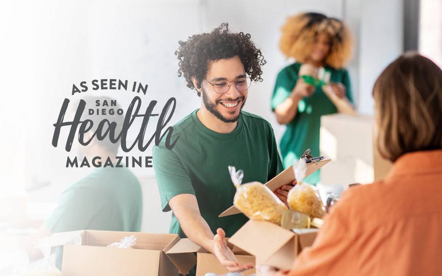 Volunteers wearing green shirts smile as they accept holiday donations - SD Health Magazine