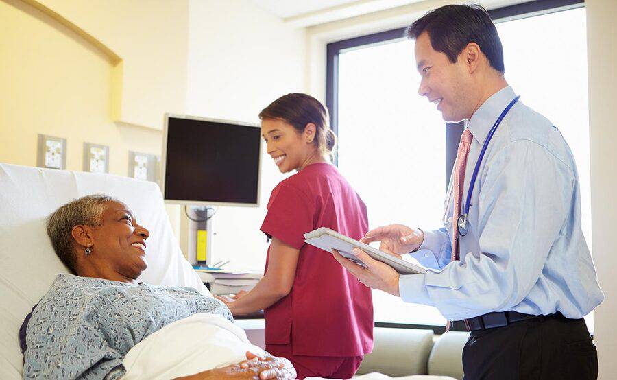 A physician and nurse talk with a mature female patient in a hospital bed, representing the MIGS fellowship at Scripps.