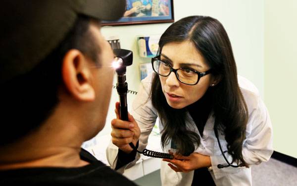 A Scripps Clinic internal medicine resident shines a light into a patient's mouth, representing the hands-on, patient-centered graduate training at Scripps.