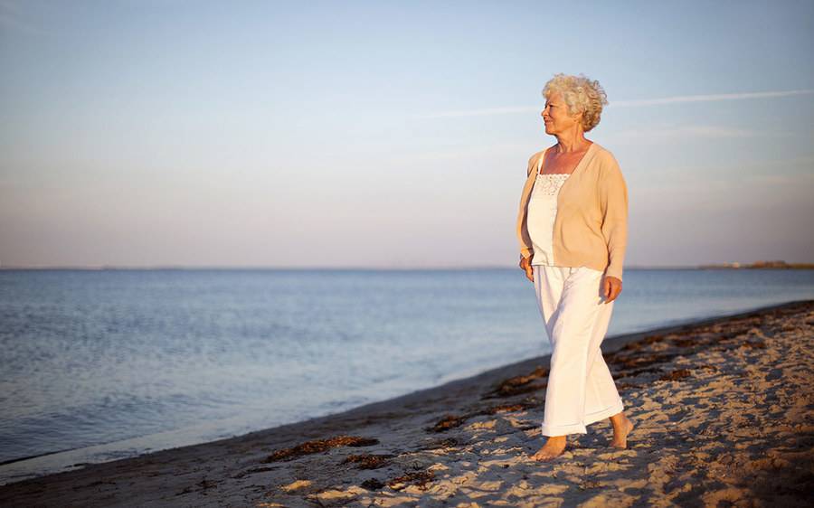 A mature woman walks along the shoreline, representing life with joint pain.