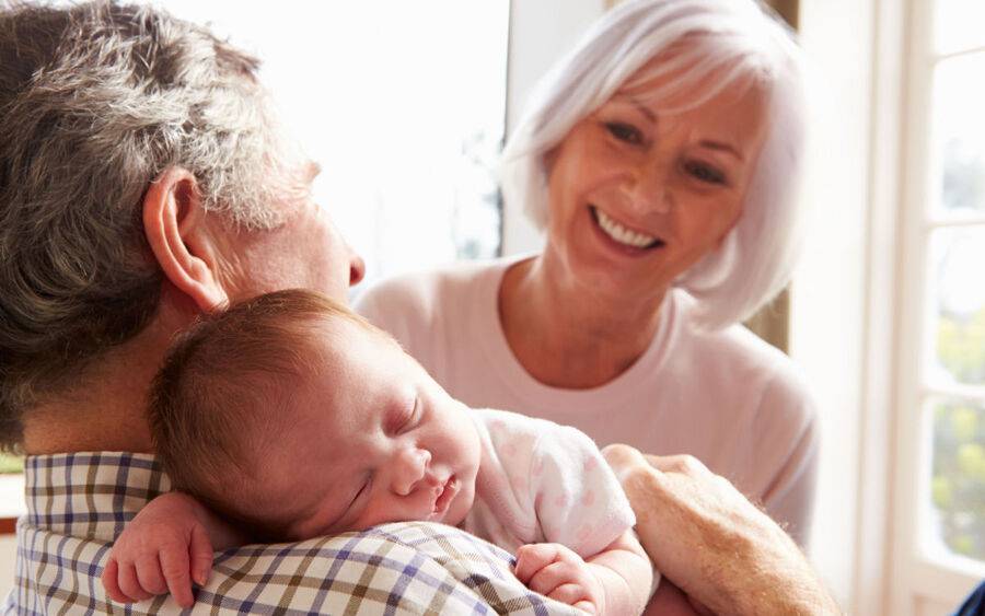 Grandmother looks at her husband holding their newborn grandchild.