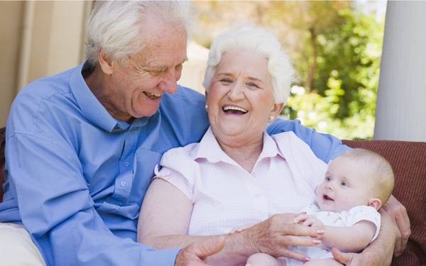 Two smiling grandparents hold a young infant, representing modern families.