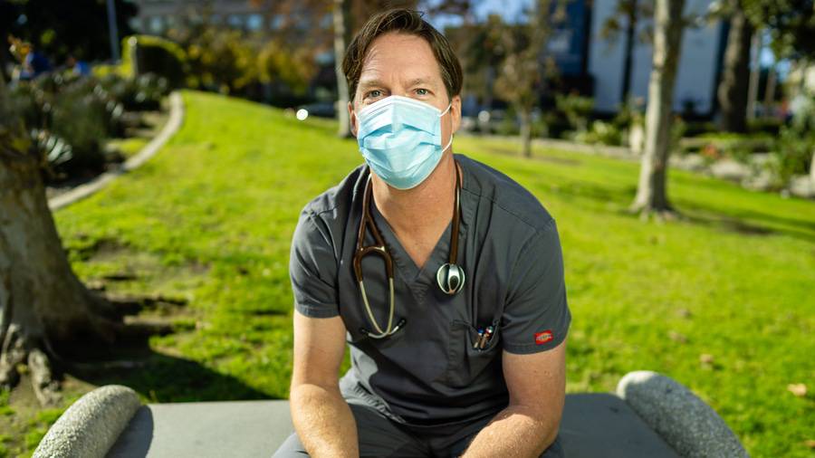 Greg Knight, RN sitting outside on a bench with his face mask on and stethoscope around is neck, one of the eight Scripps Nurses of the Year 2020. 