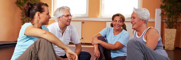 Group of four adults smiling and talking about health in a yoga studio environment.