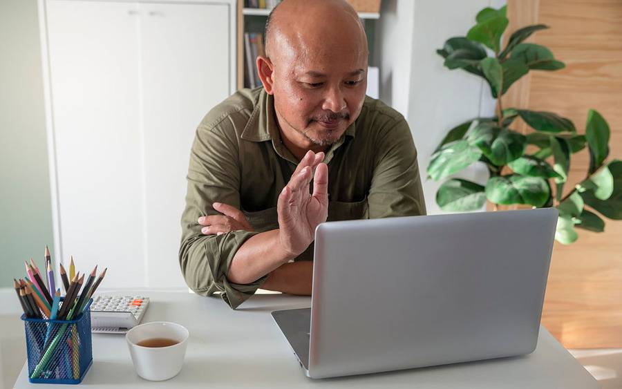An Asian man raises his hand while participating in a virtual support group.