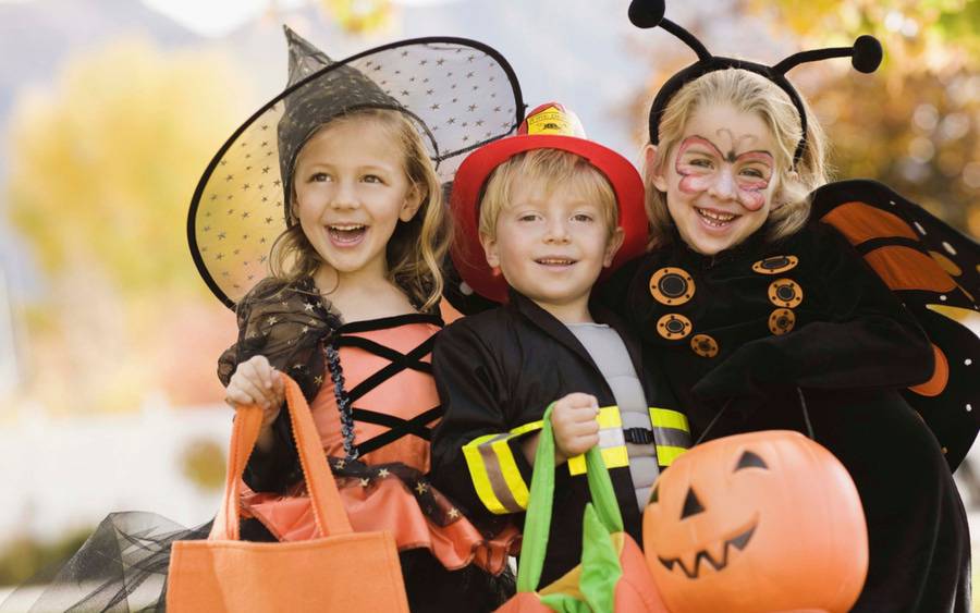 Three children dressed as a witch, firefighter and lady bug get ready to trick or treat.