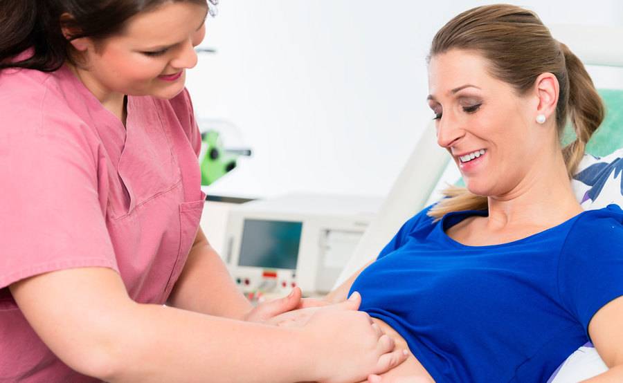 A medical professional examines a pregnant woman who is lying in a hospital bed, representing comprehensive prenatal care at Scripps.