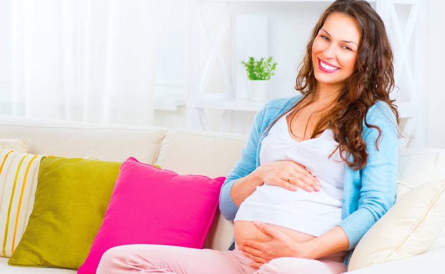 A pregnant woman smiles and sits on a couch, representing the comfortable environment at Scripps for delivering your baby.