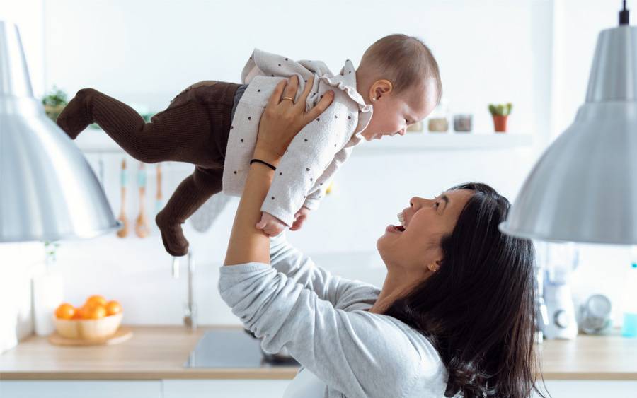 A mother lifts her baby into the air, smiling with joy. 