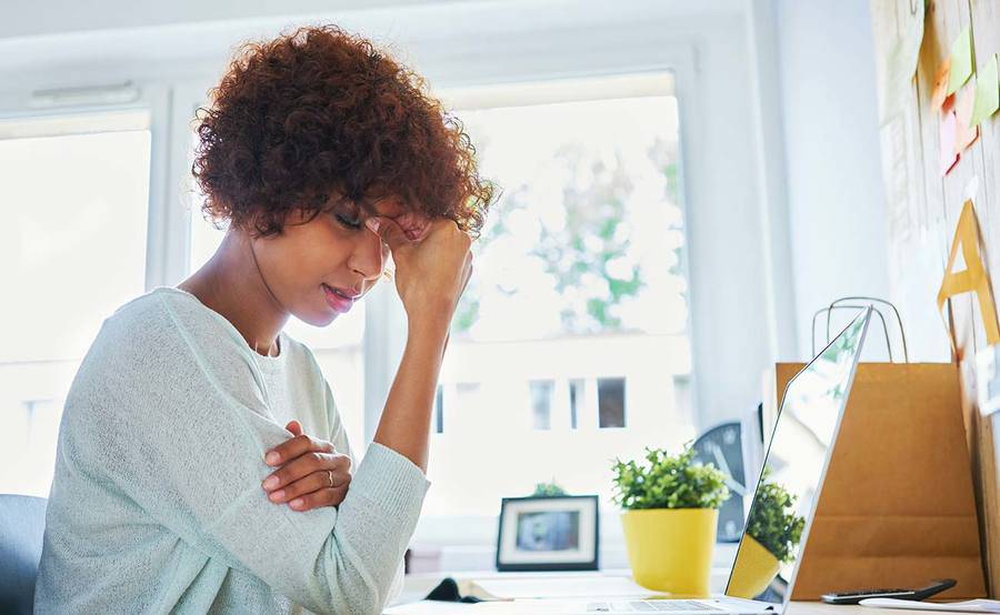 A middle-aged woman pinches the bridge of her nose, representing how headache and migraine pain can interrupt your life.