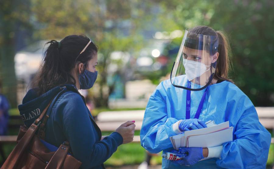 Health care worker in PPE conducts COVID screening.