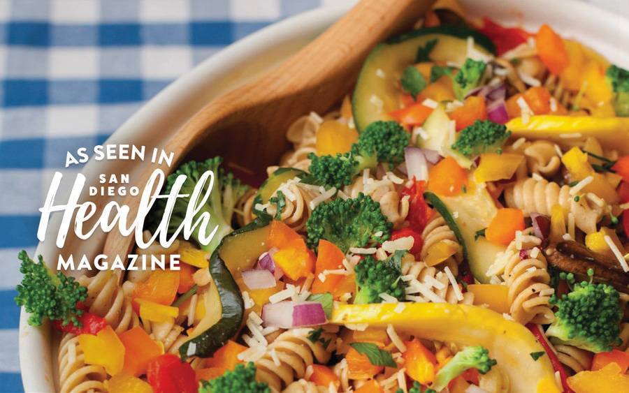 A healthy pasta salad in a bowl, including zucchini, bell peppers, broccoli and grated cheese.