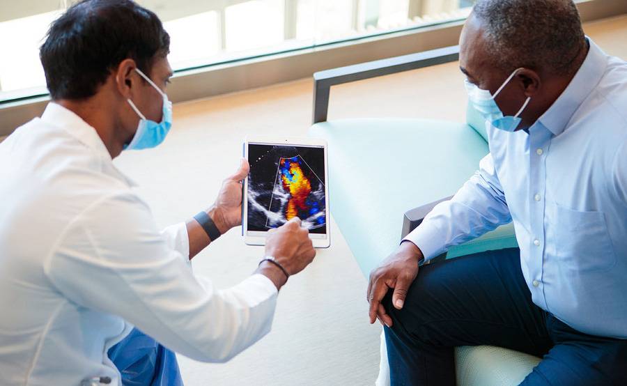 A male doctor in a white coat communicates aspects of heart failure and treatment to a black male patient,