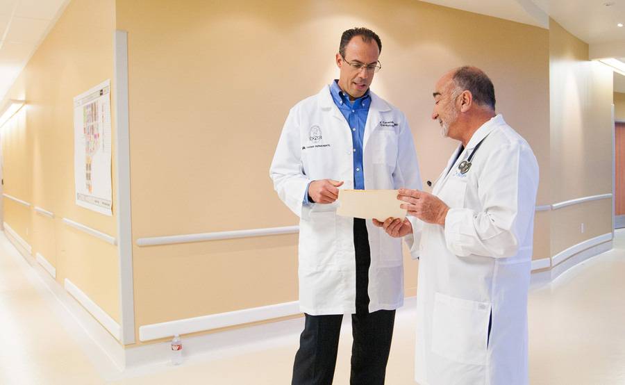 Two male cardiologists  confer patient notes in in a hospital hallway as part of the Scripps Kaiser Permanente partnership.