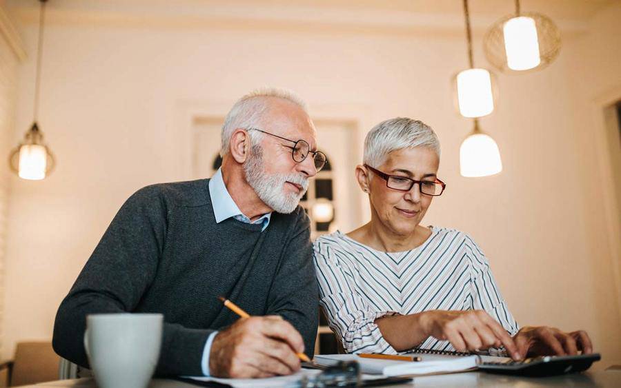 A mature couple uses a calculator to consider insurance costs, representing how to choose a Medicare plan at age 65.