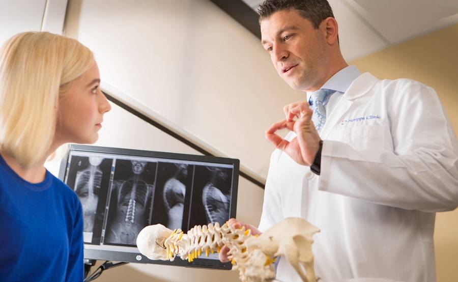 Pediatric spine surgeon Dr. Greg Mundis talks with a young patient while holding a plastic model of the backbone.