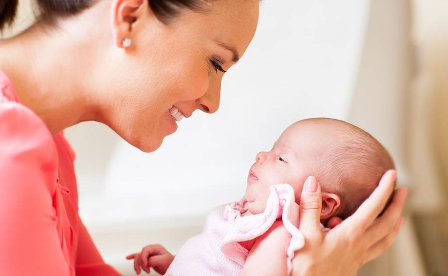 A mother smiles while holding and looking at her baby.