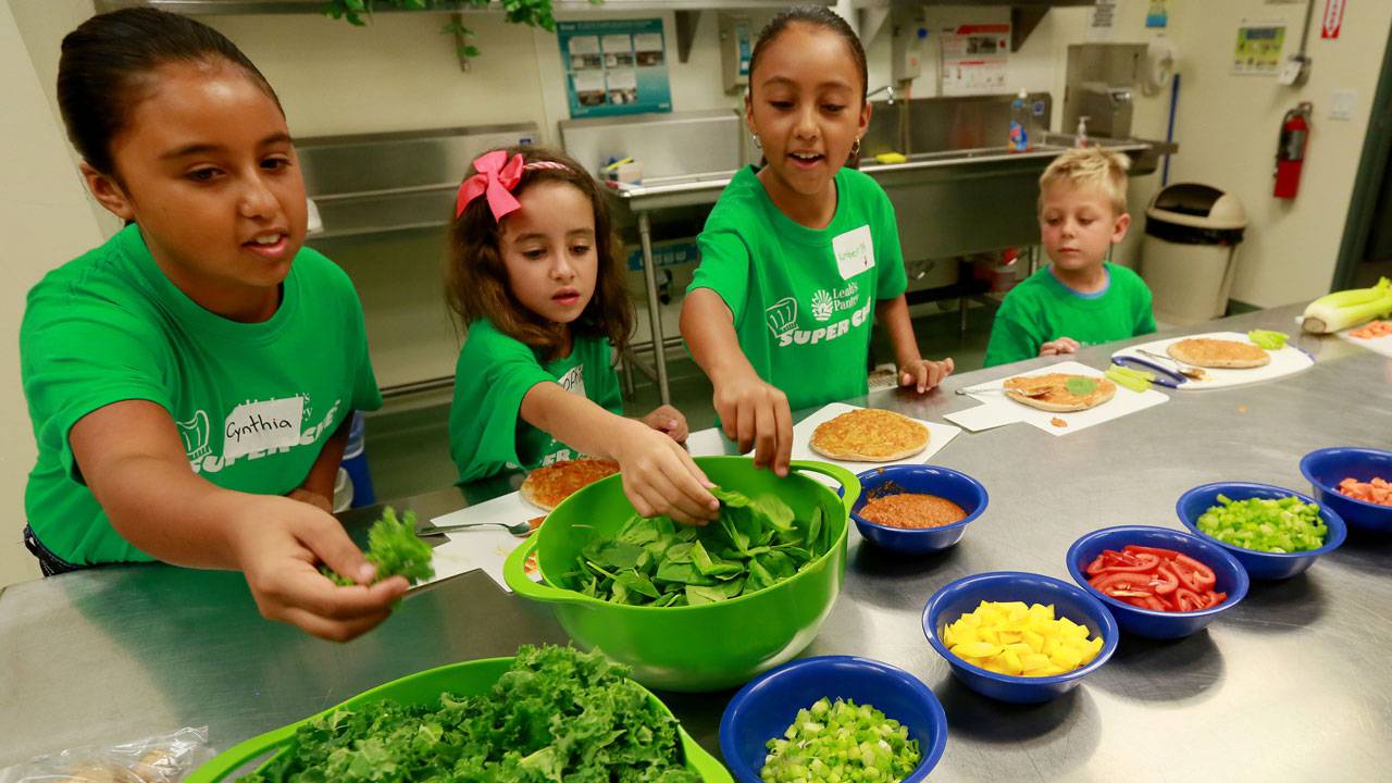Four young children choose fresh veggies to top a tortilla in a Scripps cooking class.