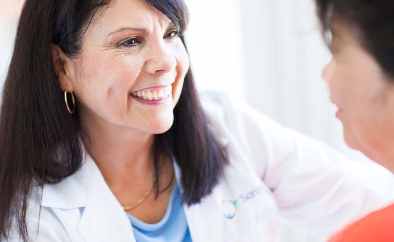 Dr. Josefina Trausch smiles while talking with a patient in a bright room, representing the warm, compassionate care at Scripps Coastal Medical Center.