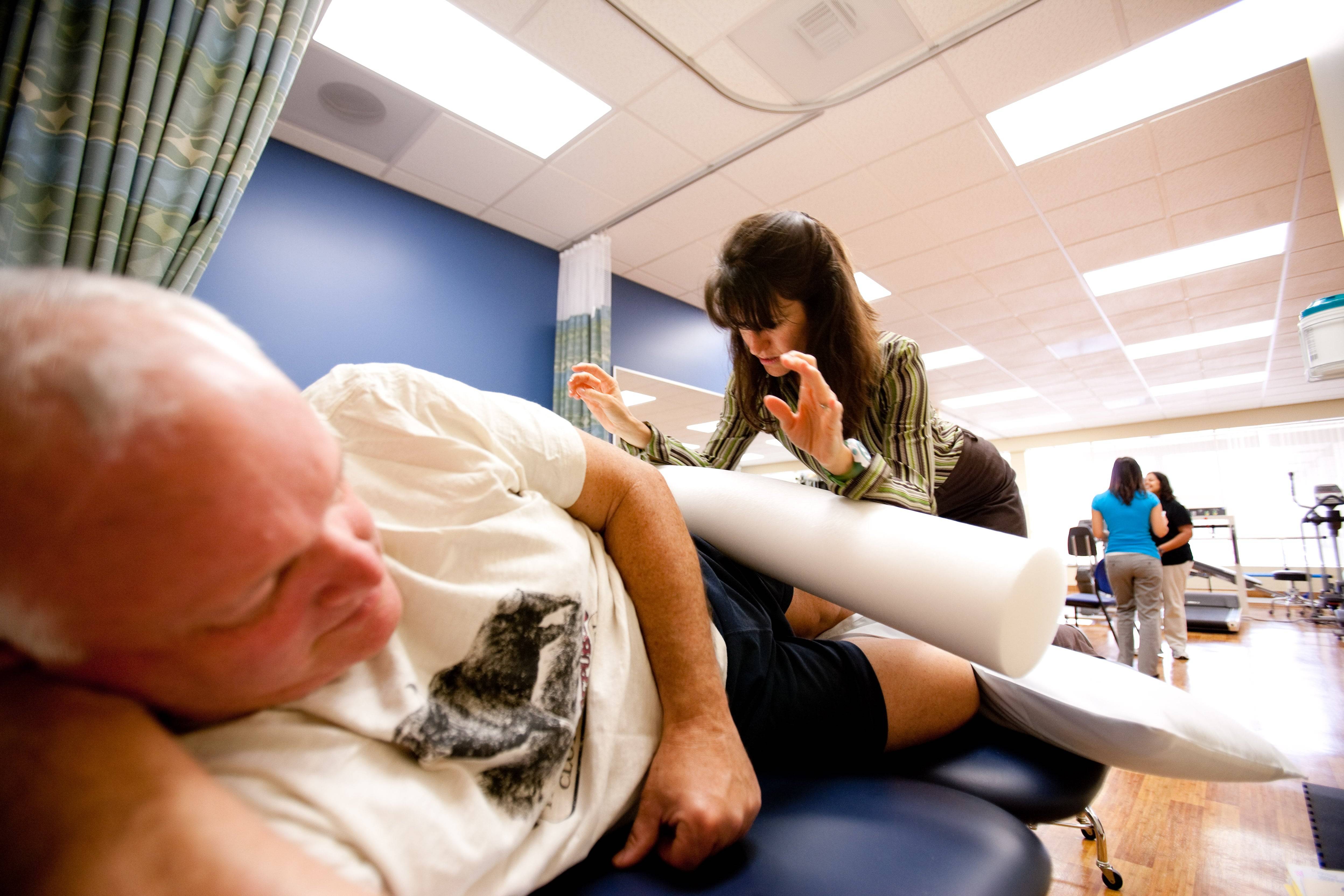 A Scripps physical therapy expert provides care to a reclining patient using a foam roller in a clinical setting.