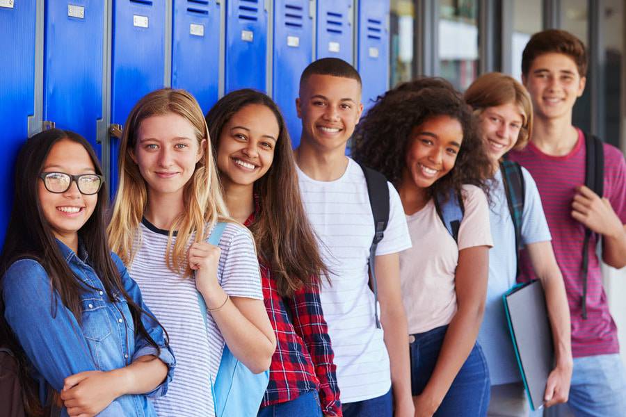 A group of high school students smile as they stand by their lockers at school showing one of the benefits of volunteering - to make new friends.