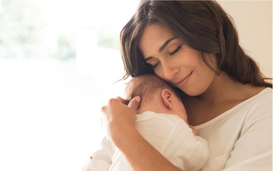 A Latina mother holds her newborn baby close to her chest.