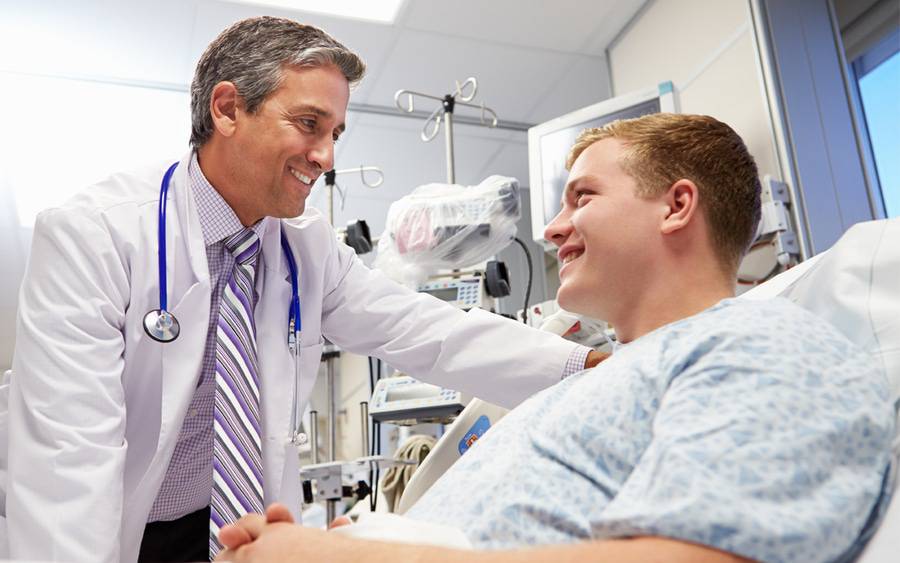 A patient in a hospital bed smiles as he talks to a doctor.