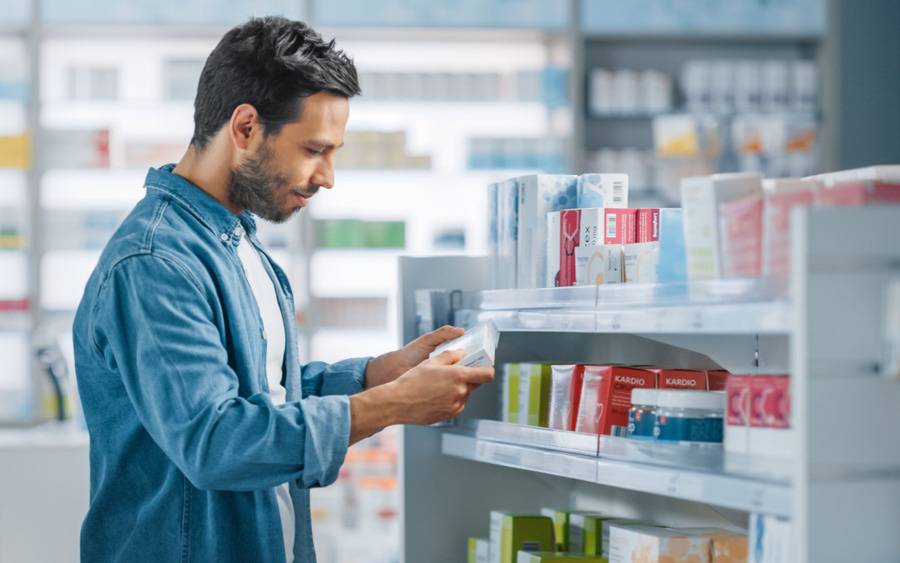 A man reads label on package in over-the-counter medicine section of store.