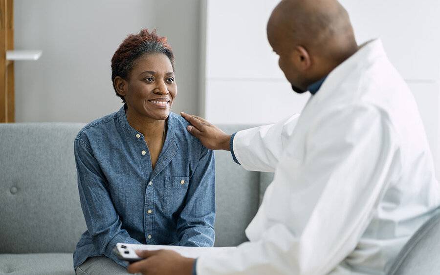 A black woman in a denim shirt is comforted by a black male doctor, representing colon cancer awareness month.