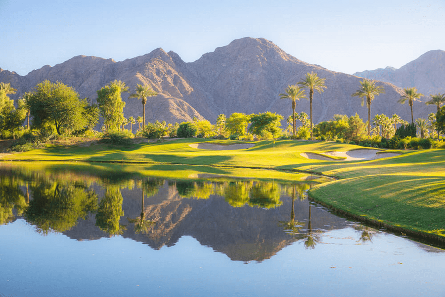 An Indian Wells golf course with mountains in the background reflect in a lake.