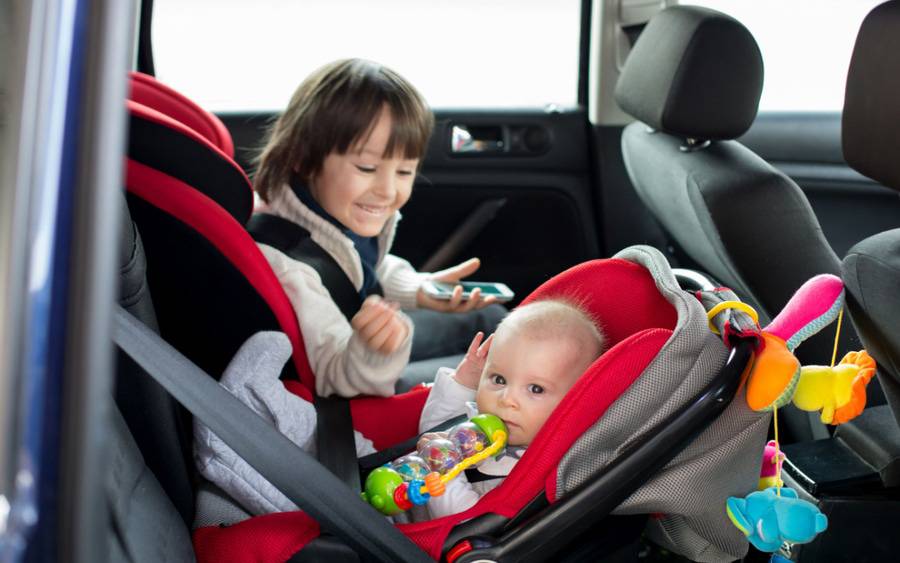 A young child in car safety seat looks at sibling in rear-facing car seat.