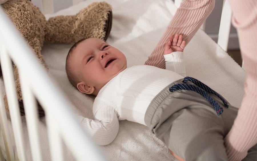 An infant with colic cries in his cribe.